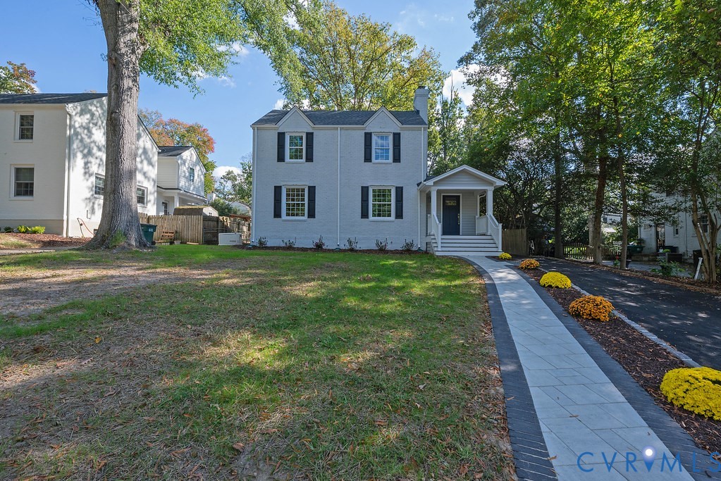 Two-story home with painted brick exterior, gabled roofline, dark shutters, covered front porch, and stone-paved walkway