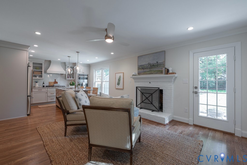 Open-concept interior featuring wood-finish flooring, a white painted brick fireplace, recessed lighting, a modern ceiling fan, and a glass-paneled exterior door
