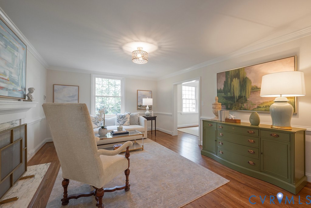 Living area featuring wood-finish flooring, crown molding, chair rail trim, and a fireplace with a stone-finish hearth