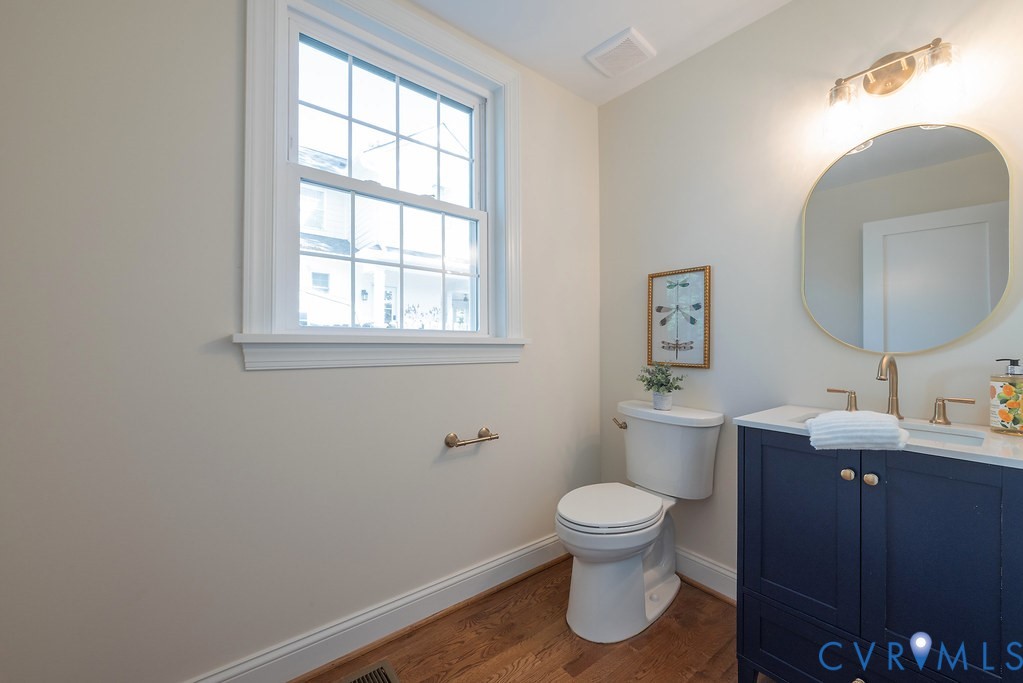 Navy blue vanity with light-toned countertop, oval-shaped wall mirror, wood-finish flooring, and metal finish hardware