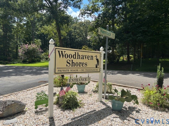 Woodhaven Shores community entrance featuring signage, paved asphalt roadway, and mature perimeter trees