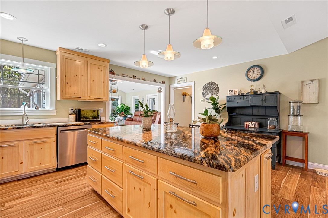 Kitchen featuring a center island with a stone countertop, light wood cabinetry, stainless steel dishwasher, and wood-finish flooring