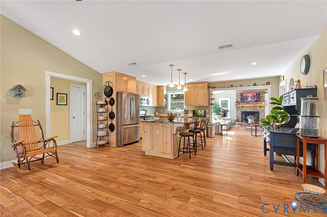 Open-concept kitchen featuring natural wood cabinetry, a central island with a countertop, stainless steel appliances, recessed lighting, and wood-finish flooring