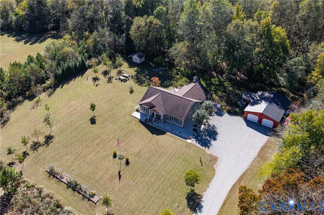 Expansive parcel featuring a detached two-car garage, gravel driveway, mature perimeter trees, and a rectangular garden bed