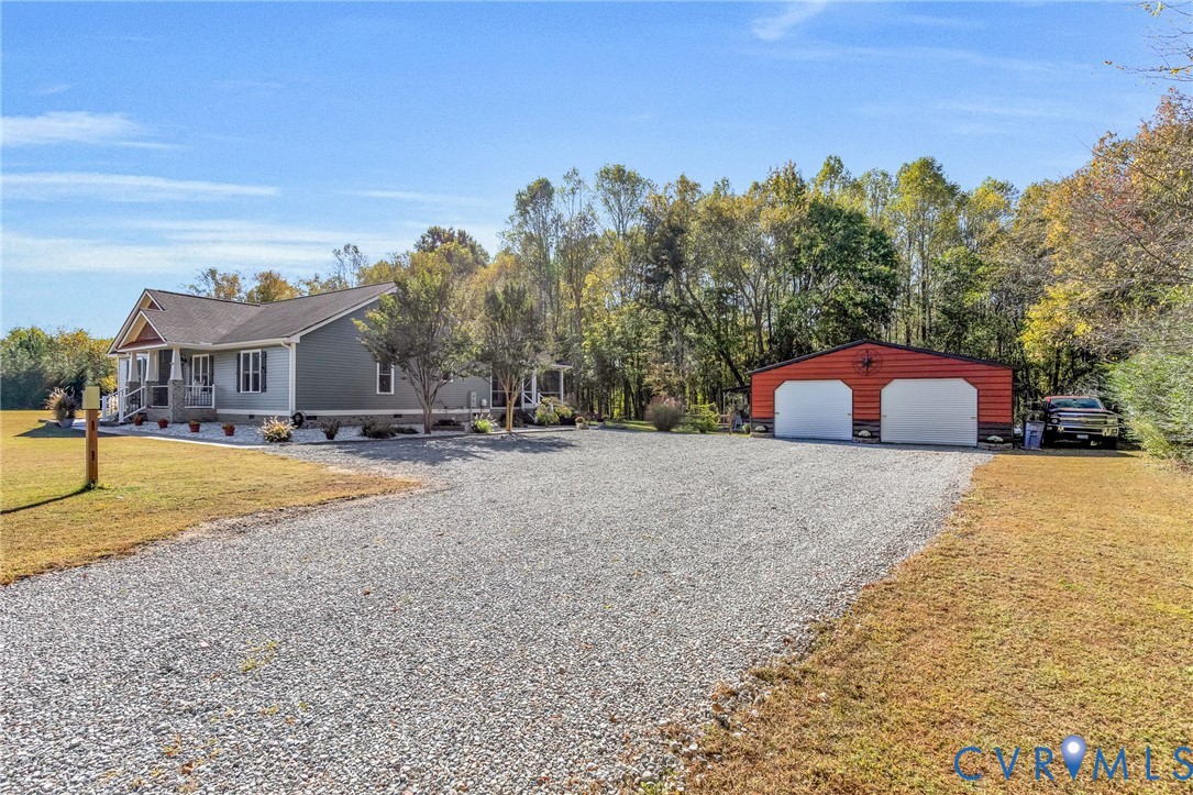 Single-story residence with lap siding, covered front porch, stone-veneer foundation accents, gravel driveway, and detached two-car garage