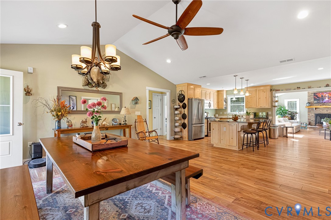 Vaulted ceilings, open-concept kitchen with light wood cabinetry, wood-finish flooring, multi-light chandelier, and stone-surround fireplace