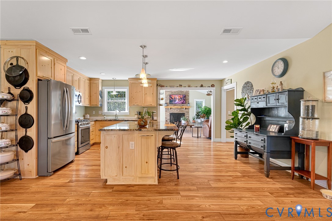 Kitchen featuring light-finish cabinetry, a stone-topped central island with bar seating, stainless steel appliances, and wood-finish flooring