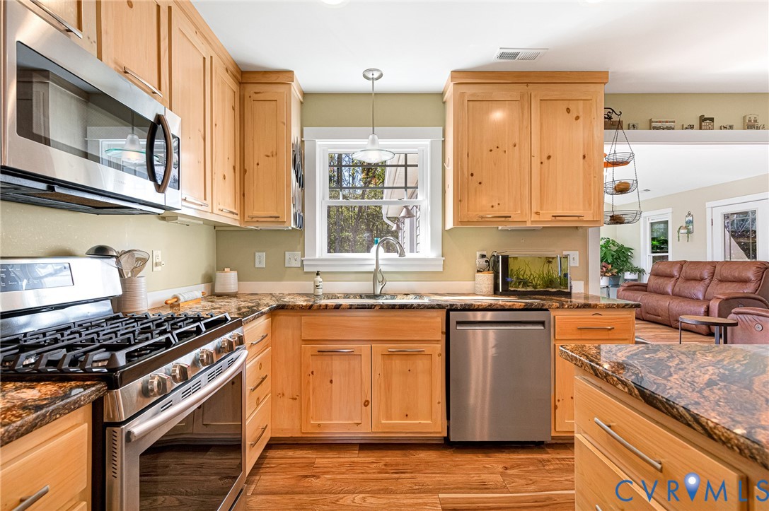 Kitchen featuring natural wood cabinetry, stone-surface countertops, stainless steel appliances, a double-basin sink with a gooseneck faucet, and wood-finish flooring