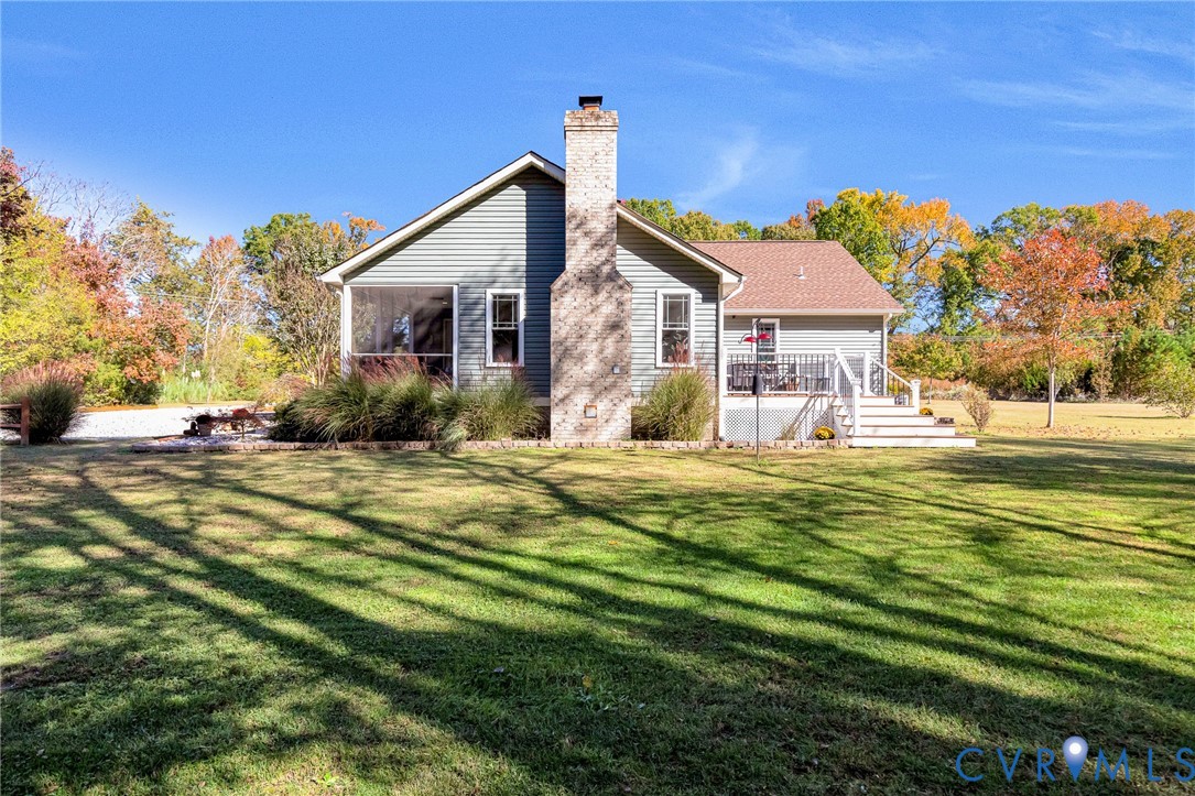 Exterior featuring horizontal siding, a central masonry chimney, a screened porch, a raised deck with staircase, and extensive lawn
