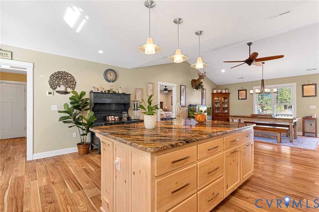 Kitchen featuring a natural stone countertop island, light-finish cabinetry, vaulted ceilings, three pendant lights, and wood-finish flooring