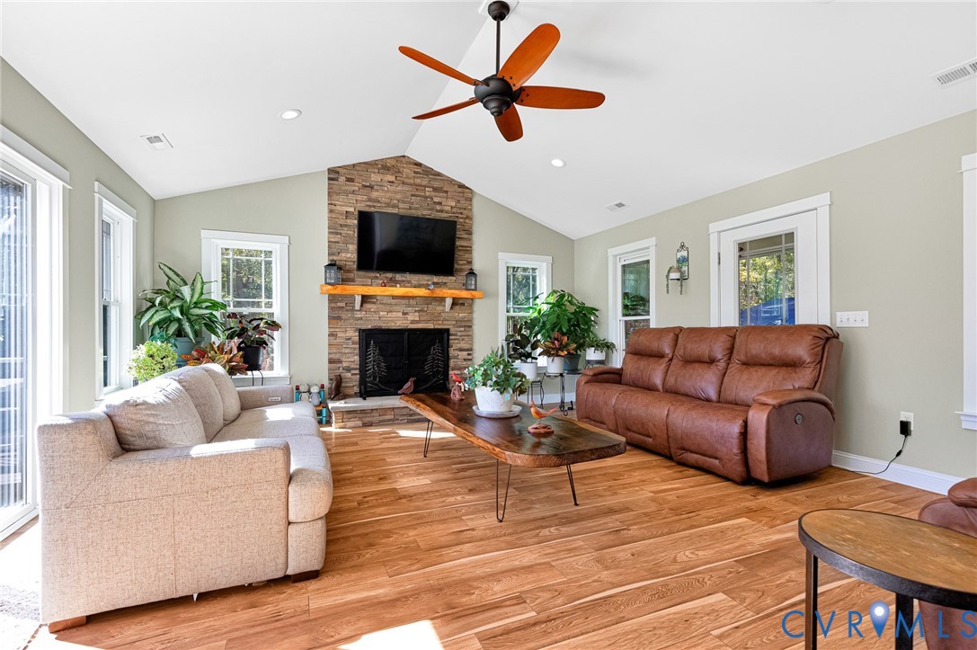 Vaulted ceiling featuring a stacked stone fireplace with a natural wood mantel, wood-finish flooring, and a ceiling fan