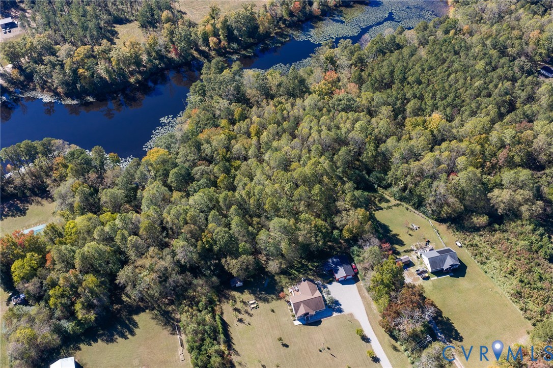 Aerial perspective of a sprawling property featuring mature forest canopy, direct water frontage, expansive cleared acreage, paved private driveway, and residential structures with shingled roofing