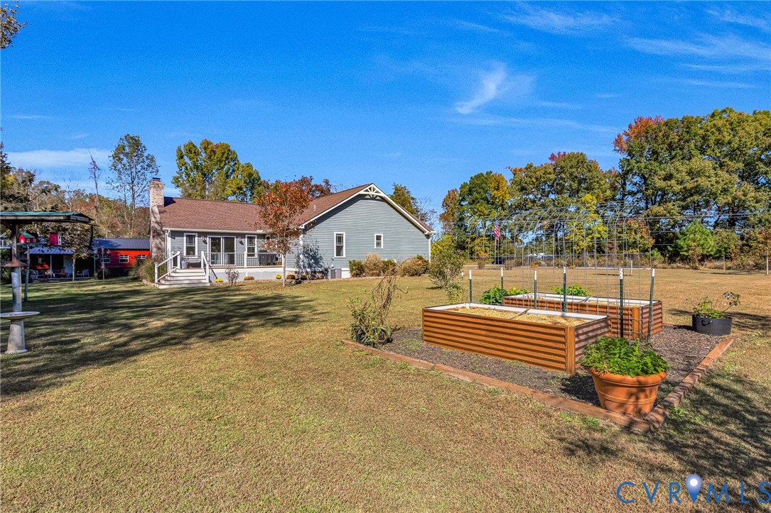 Expansive backyard featuring raised metal garden beds, masonry-bordered landscaping, an attached rear deck with stairs, and exterior horizontal siding