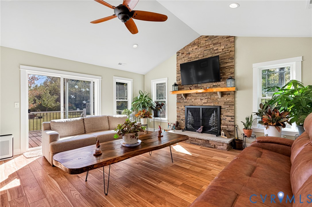 Vaulted ceilings, stacked stone fireplace with natural wood mantel, wood-finish flooring, ceiling fan, and sliding glass doors