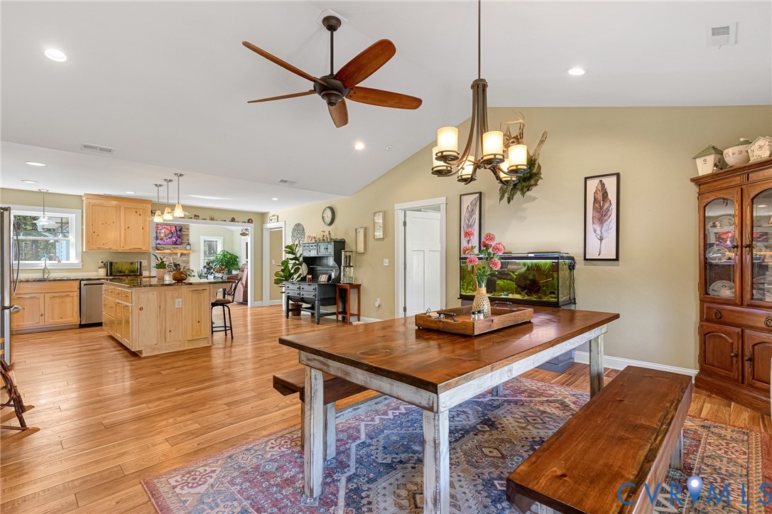 Vaulted ceilings with recessed lighting, wood-finish flooring, a multi-arm chandelier, ceiling fan, and cabinetry with stone countertops
