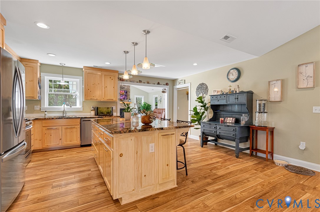 Kitchen featuring natural finish wood cabinetry, stone countertops, a central island with pendant lighting, stainless steel appliances, and wood-finish flooring