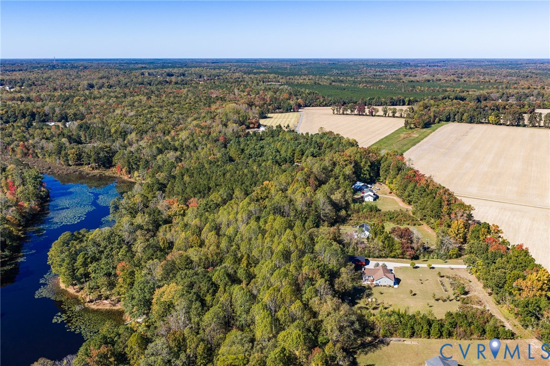 Aerial perspective of rural acreage featuring a natural water body, expansive woodland, and open fields