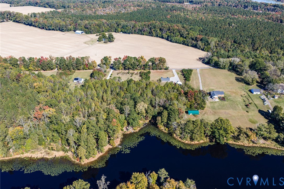 Aerial perspective of extensive acreage featuring mature tree lines, open pasture, and substantial waterfront access