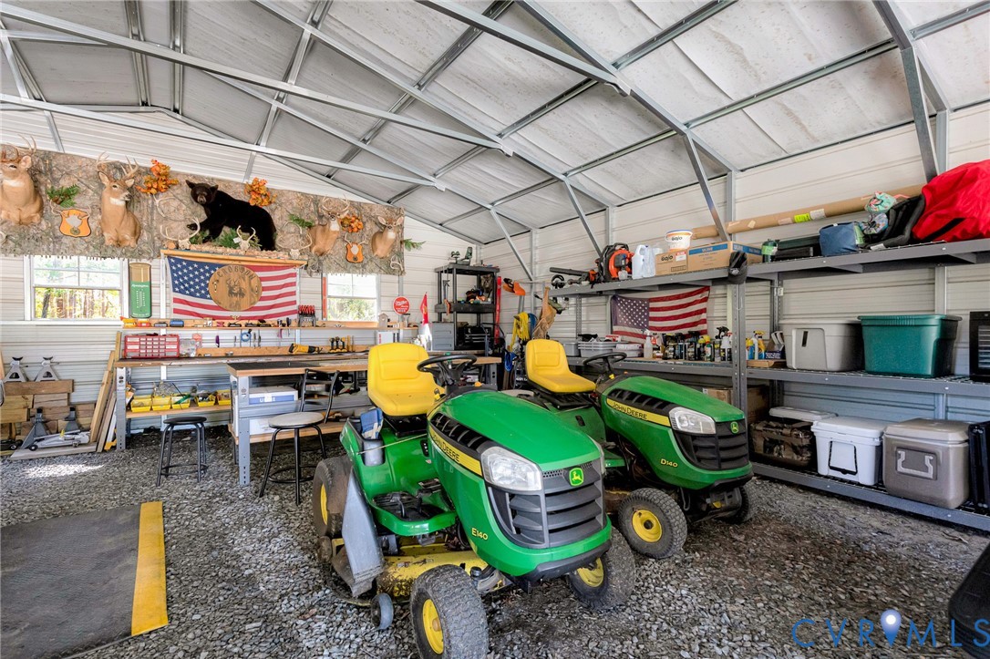 Metal-frame workshop featuring a vaulted roof, gravel flooring, integrated workbench, and fixed metal industrial shelving units