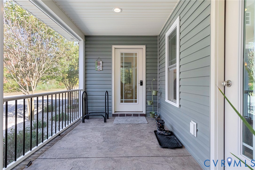 Covered porch featuring textured concrete flooring, horizontal siding, black metal railing, and a glass-paneled entry door