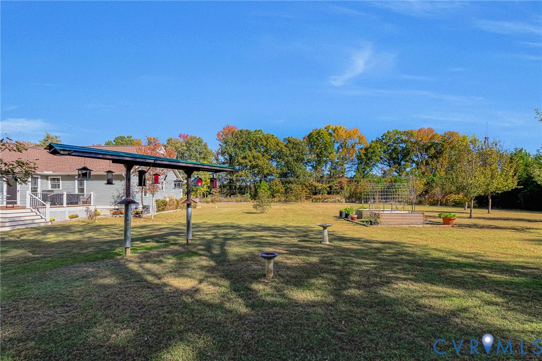 Expansive backyard featuring a large grass lawn, mature trees, a metal trellis structure, and a raised garden bed