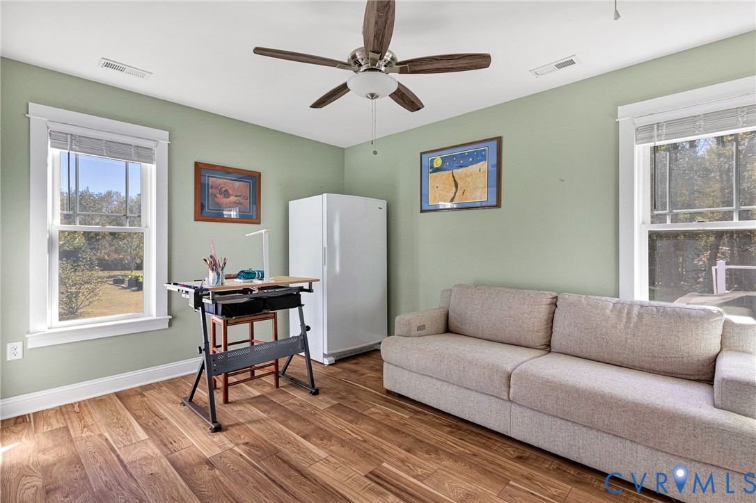 Room featuring wood-finish flooring, dual windows with white casing, and a multi-blade ceiling fan with central lighting