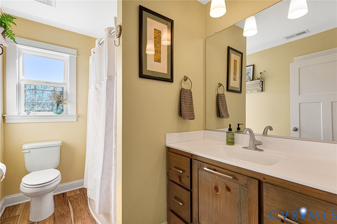 Bathroom featuring a wood-finish vanity with a white countertop, an integrated sink with a metallic faucet, a full-width wall-mounted mirror, and wood-finish flooring