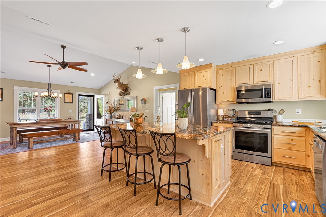 Kitchen featuring light-tone wood cabinetry, natural stone countertops, stainless steel appliances, pendant lighting, and wood-finish flooring