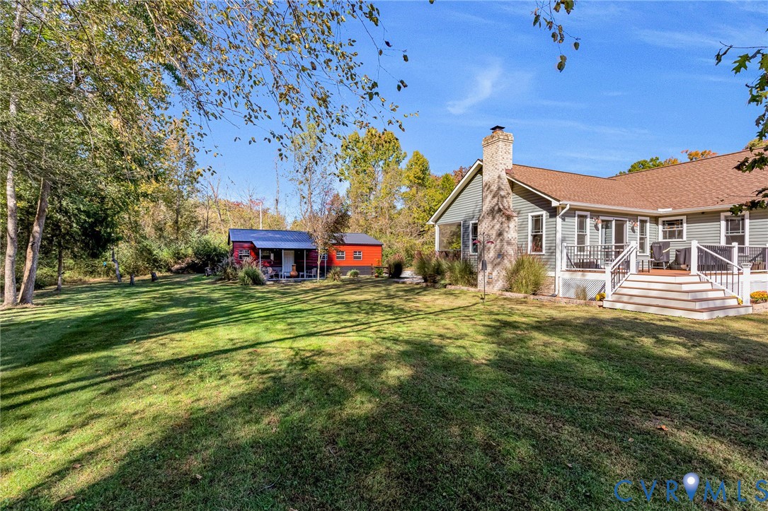 Expansive backyard featuring a manicured lawn, stone-veneer chimney, elevated rear deck with white railing, and detached outbuilding