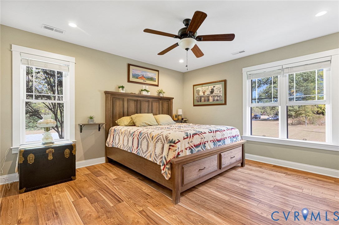 Neutral-toned bedroom featuring wood-finish flooring, recessed lighting, a ceiling fan with integrated light, and large windows with white trim