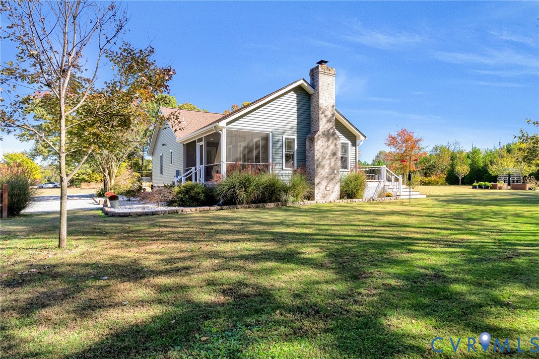 Siding exterior featuring a prominent stone-finish chimney, a screened-in porch, an elevated rear deck with railings, and established landscaping set on expansive grounds