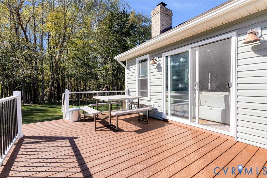 Rear exterior deck featuring composite wood-finish decking, white metal railing, and a brick chimney