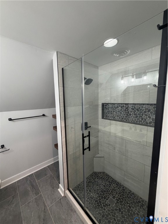 Walk-in shower featuring a frameless glass door, stone-tile flooring, horizontal wall tiling, integrated shelving niche, and matte black fixtures Walk-in shower featuring a frameless glass door, stone-tile flooring, horizontal wall tiling, integrated shelving niche, and matte black fixtures