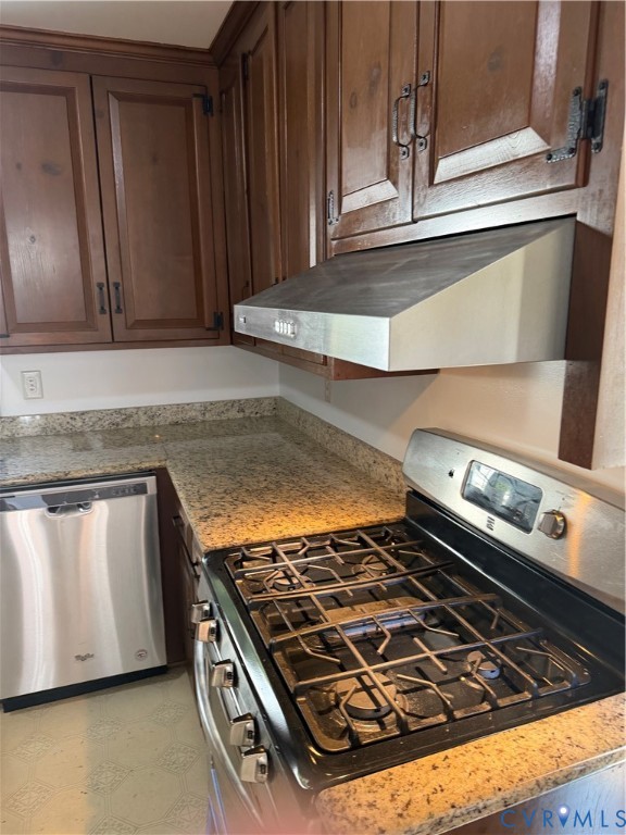 Stained wood cabinetry, stone countertops, stainless steel dishwasher, gas range, and wall-mounted stainless steel exhaust hood Stained wood cabinetry, stone countertops, stainless steel dishwasher, gas range, and wall-mounted stainless steel exhaust hood