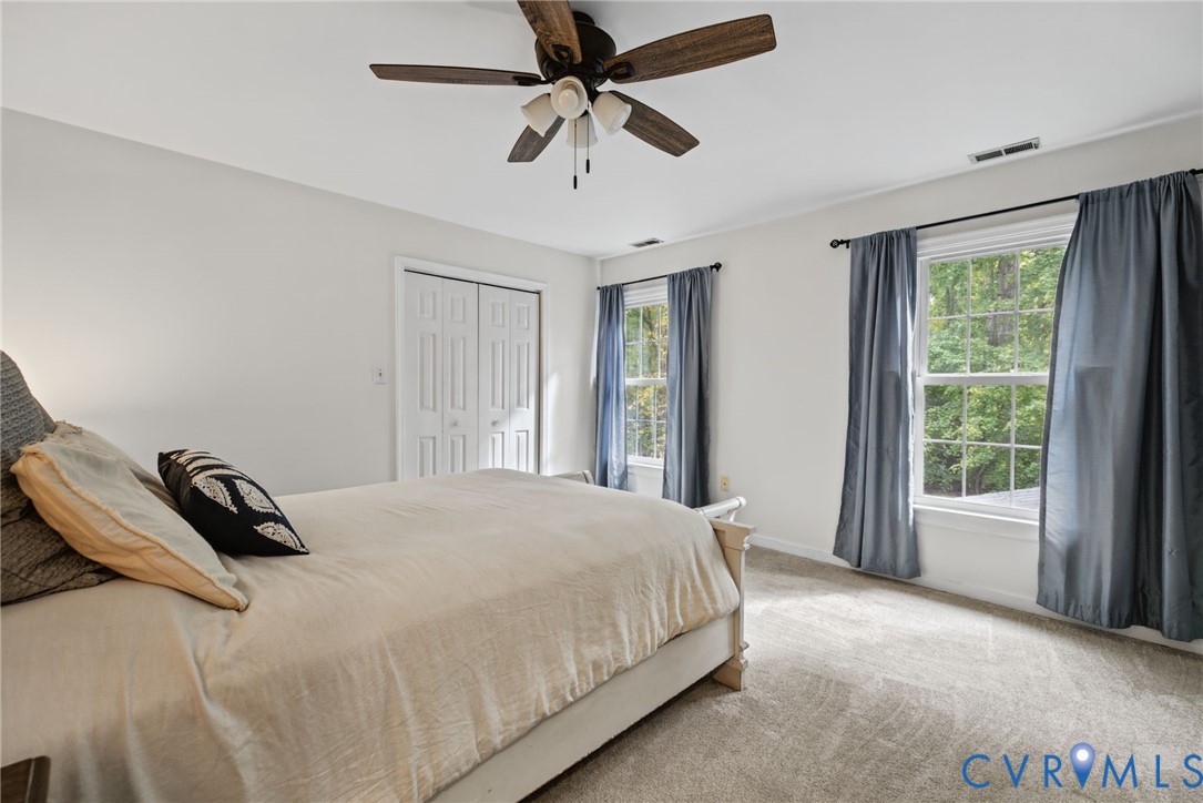 Room featuring neutral wall tones, wall-to-wall carpeting, dual windows, a ceiling fan with integrated lighting, and a double-door closet