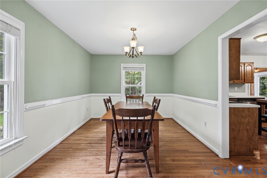 Dining area featuring wood-finish flooring, white wainscoting, a central multi-light chandelier, and windows with white casings