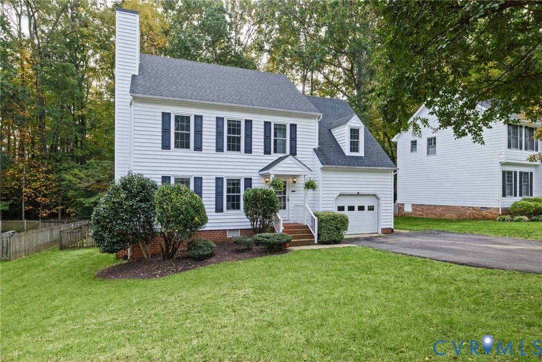 Two-story colonial exterior featuring white horizontal siding, dark shutters, a brick foundation, a front-facing gable roof, and an attached one-car garage Two-story colonial exterior featuring white horizontal siding, dark shutters, a brick foundation, a front-facing gable roof, and an attached one-car garage