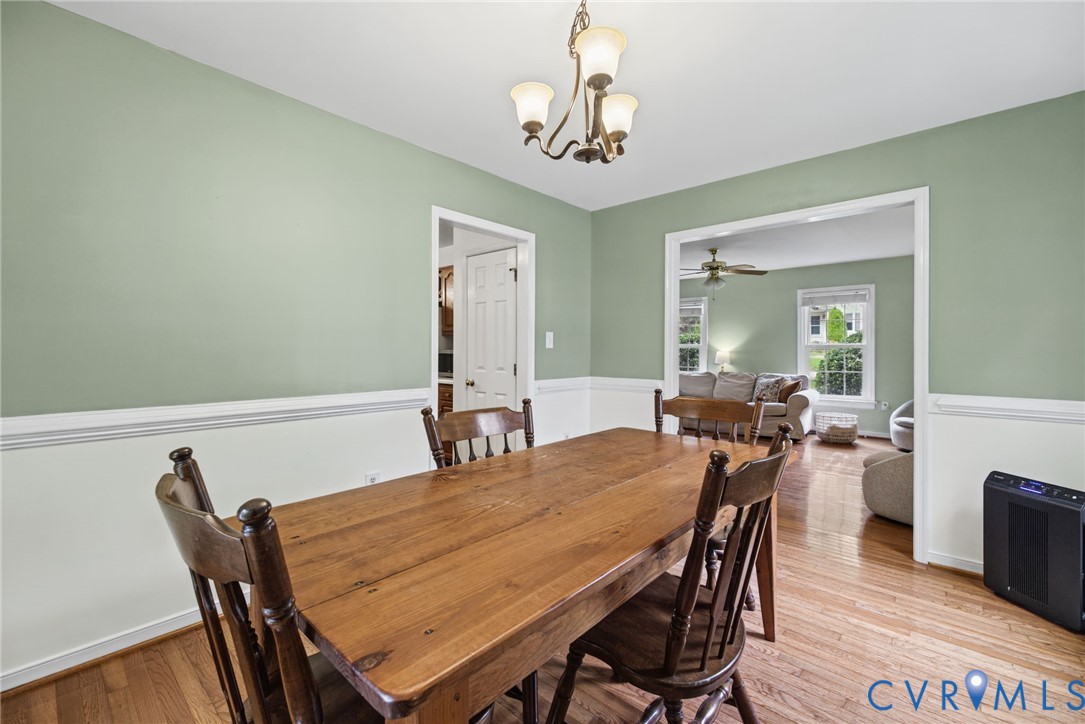 Dining area featuring wood-finish flooring, white chair rail molding, and a three-light chandelier