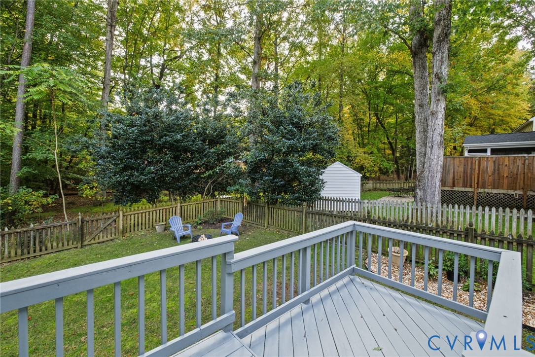 Elevated deck with painted railings, fenced backyard, mature trees, and detached storage structure