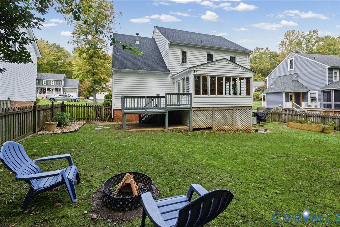 Rear elevation featuring horizontal lap siding, an enclosed sunroom, an elevated wooden deck, and a fenced backyard with a raised garden bed