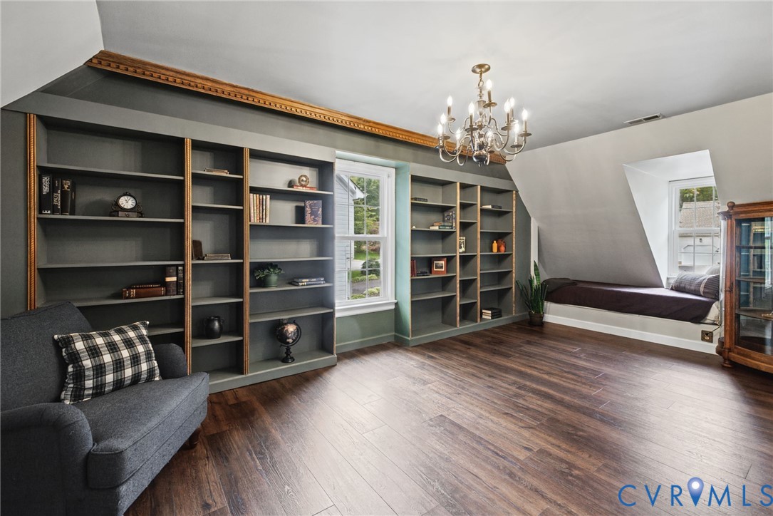 Built-in floor-to-ceiling shelving, wood-finish flooring, recessed window seat, crown molding, and multi-arm chandelier