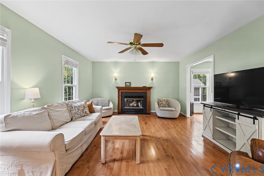 Living area featuring wood-finish flooring, a fireplace with a wooden mantel, dual wall-mounted sconces, and a ceiling fan