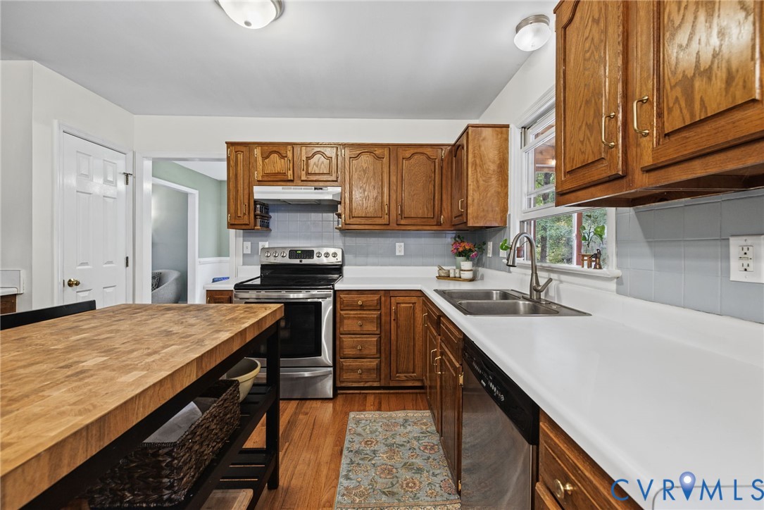 Kitchen featuring wood cabinetry, solid surface countertops, a stainless steel range, a stainless steel double-basin sink with a gooseneck faucet, and wood-finish flooring