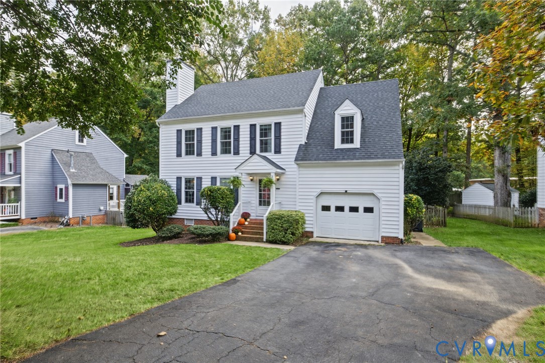 Two-story Colonial exterior featuring white horizontal siding, dark shutters, an attached single-car garage, an asphalt driveway, and a gabled dormer window