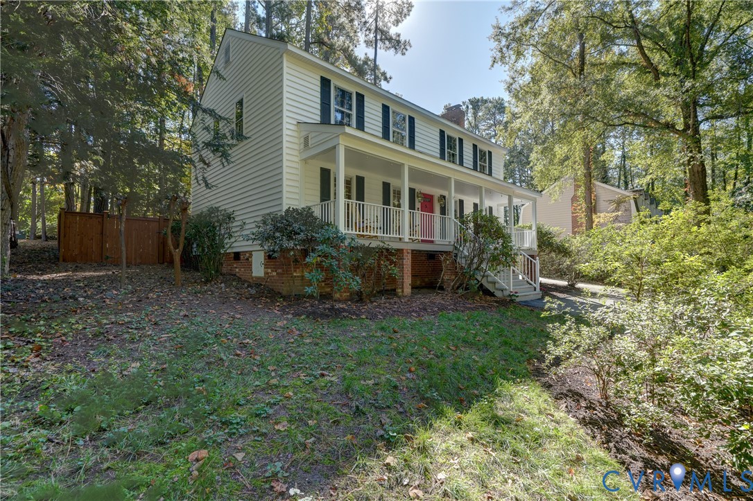 Two-story colonial-style residence featuring horizontal siding, a full-length covered front porch with white railing, and a brick foundation base Two-story colonial-style residence featuring horizontal siding, a full-length covered front porch with white railing, and a brick foundation base
