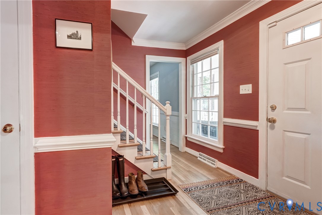 Foyer featuring textured wall finish, wood-finish flooring, white millwork including crown molding and chair rail, staircase with white balusters, and a paneled entry door with transom light