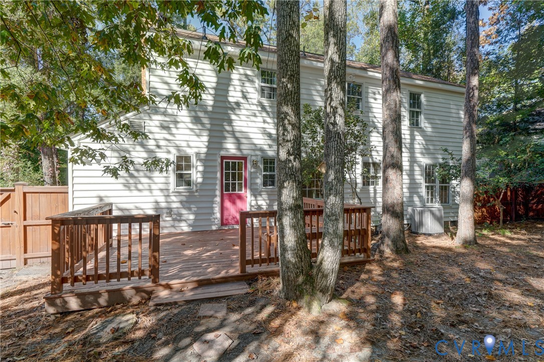 Exterior elevation featuring horizontal siding, a multi-lite door, and an elevated wood deck enclosed by a wood railing, situated on a lot with mature trees and wood perimeter fencing