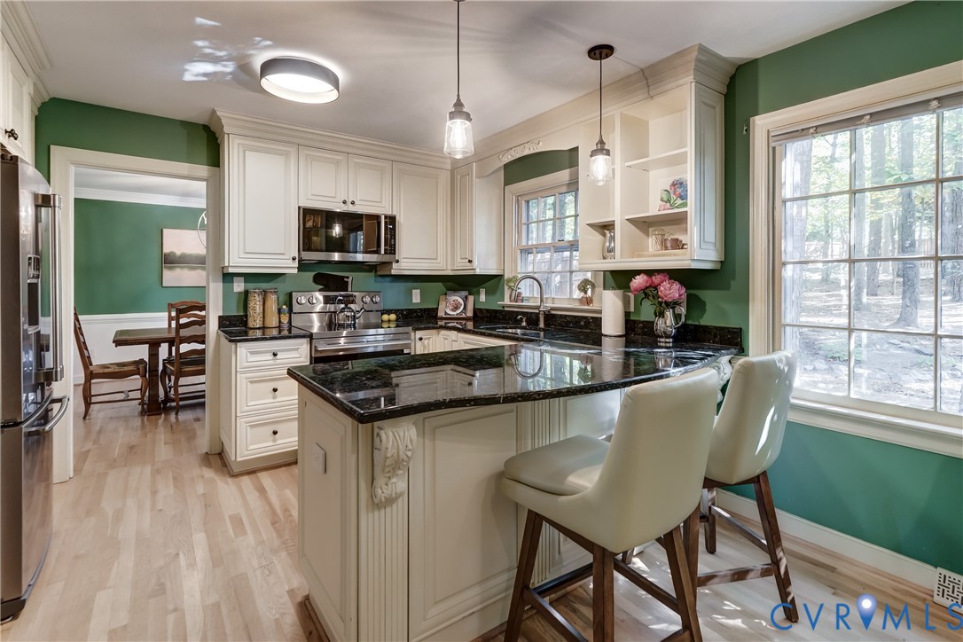 Kitchen featuring off-white cabinetry, dark stone countertops, wood-finish flooring, multi-pane windows, and pendant lighting
