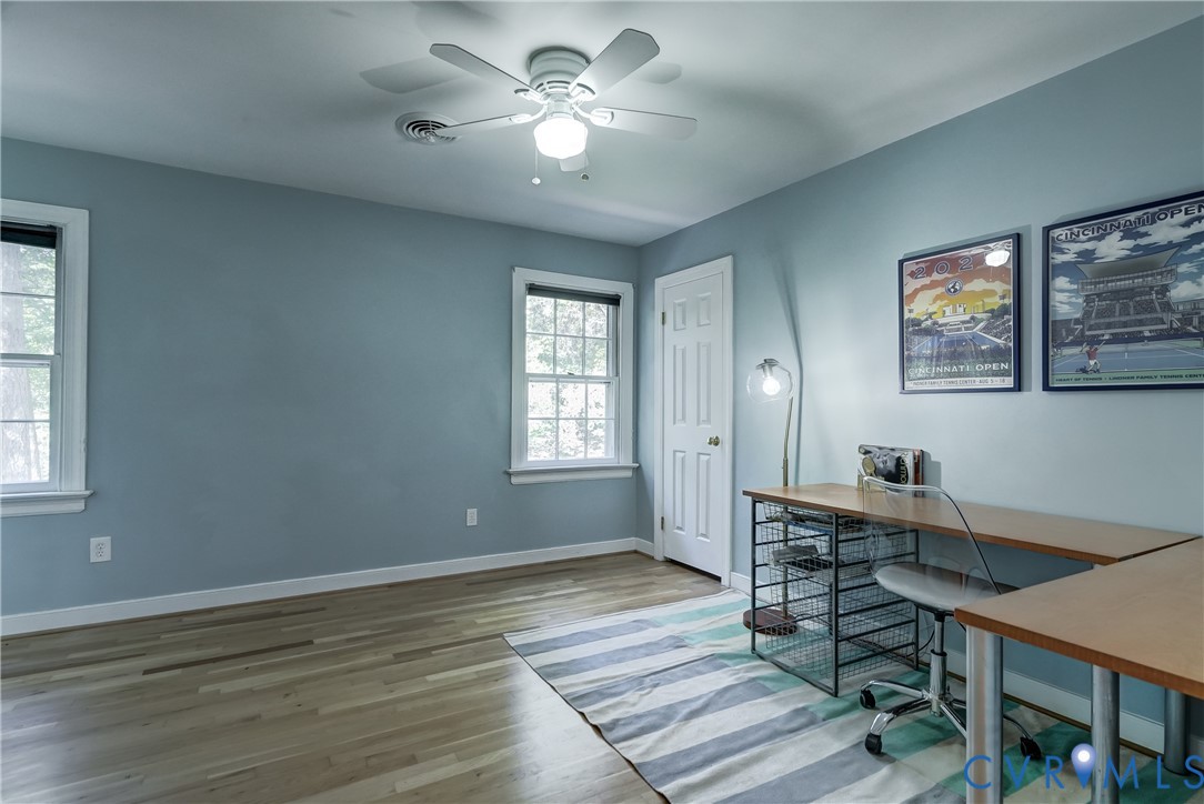 Room with wood-finish flooring, white-painted six-panel door, multi-pane windows, and a central ceiling fan with integrated lighting