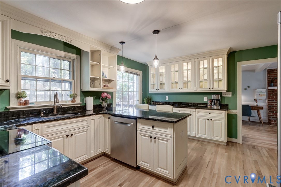 Kitchen featuring cream-colored shaker cabinetry with glass-front uppers, stone-surfaced countertops, a center island with stainless steel dishwasher, dual pendant lighting, and wood-finish flooring